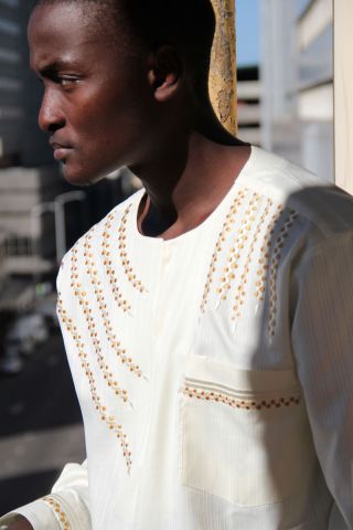 in honor of the martyred Pan-Africanist Gaddafi. This is a style on the cusp of revolutionary modern Pan-African expression with the unique modern nuanced West African embroidery. Exclusive premium fabric from Ghana is the base for this exquisite top of h
